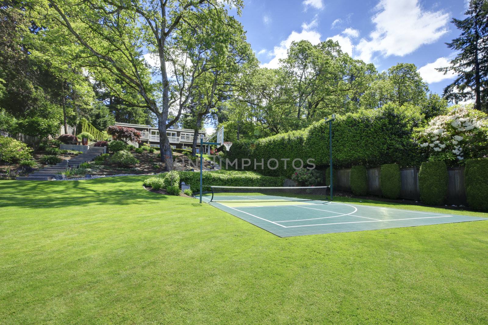 Tennis court with house on the hill and bright green grass.