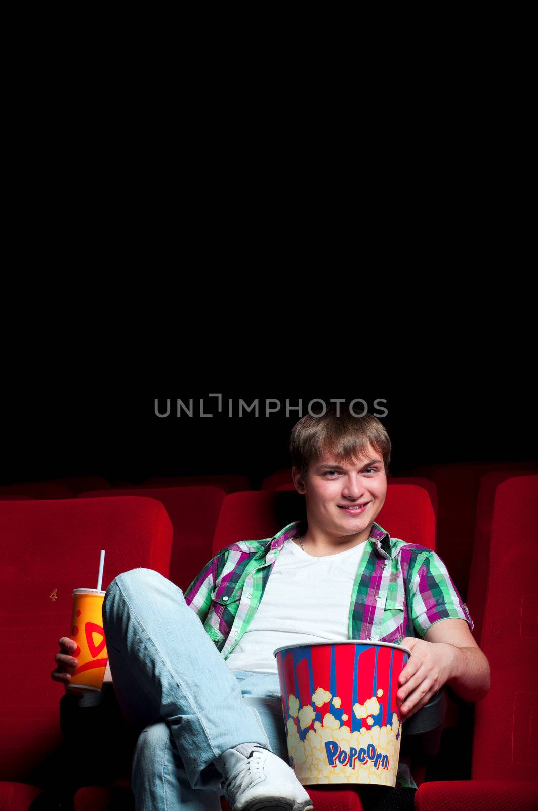 man in a movie theater, watching a movie and drink a drink