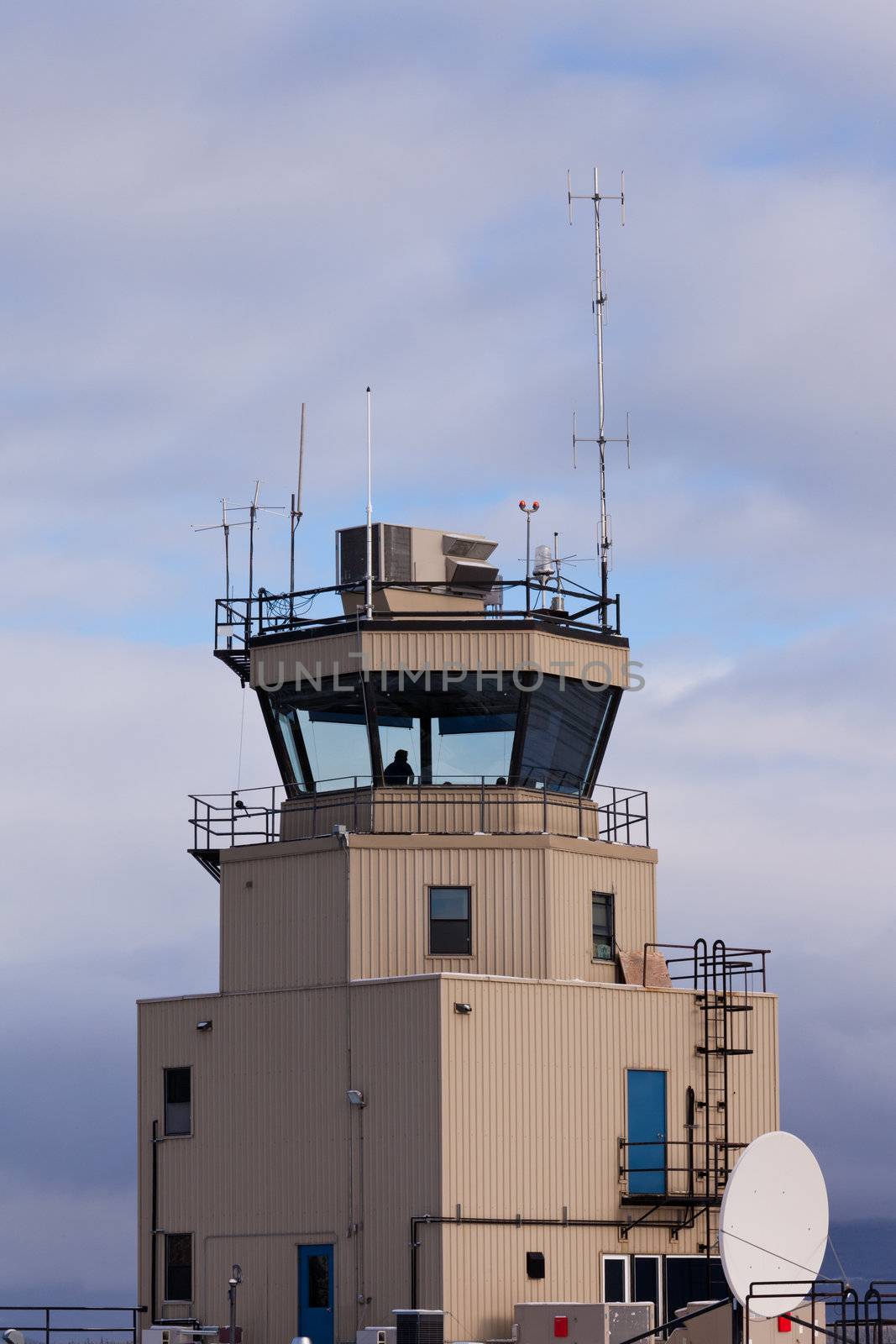 Small airport air traffic control tower with silhouette of man behind huge glass windows monitoring the airfield
