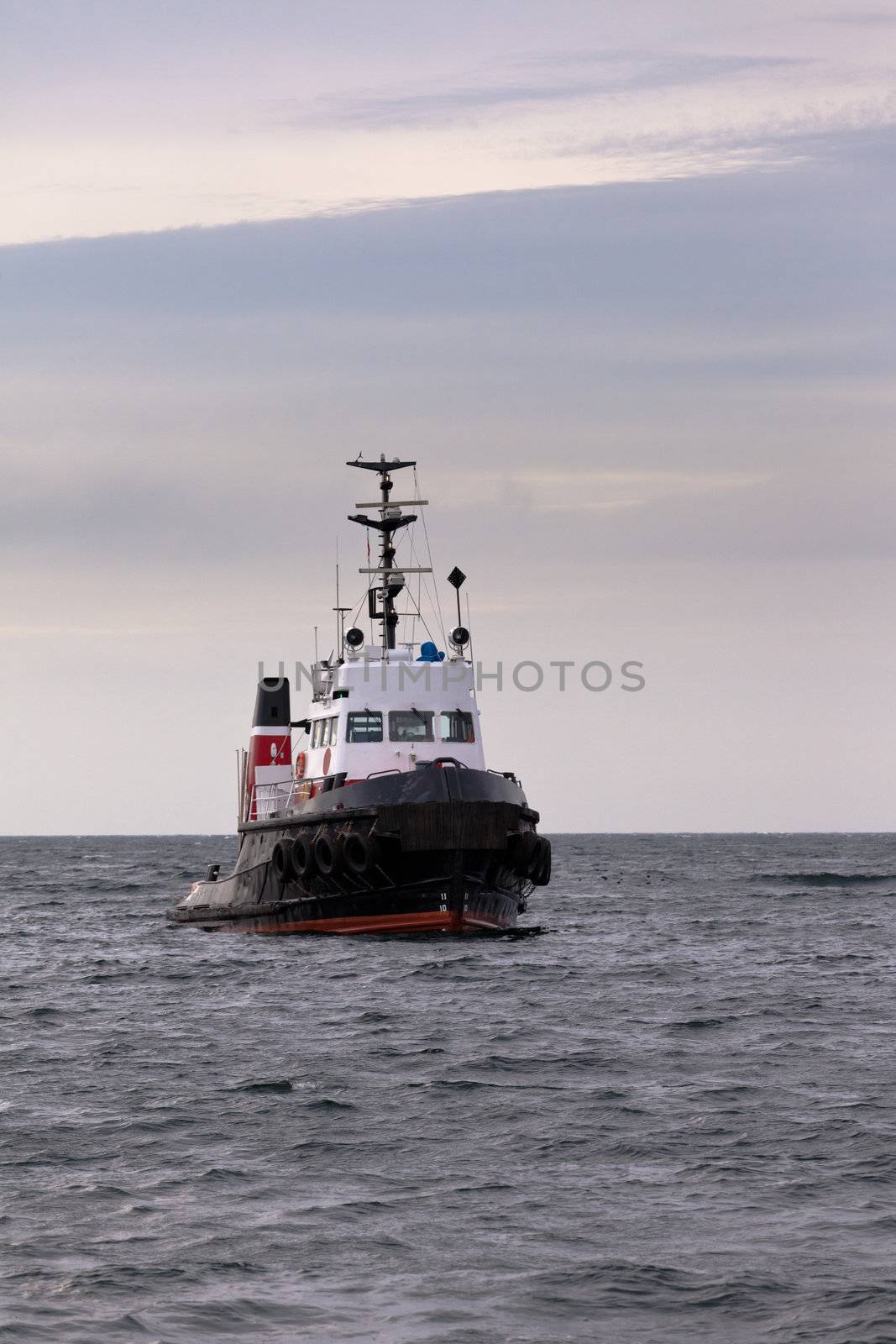 Tugboat floating in wait on calm ocean at anchor by PiLens