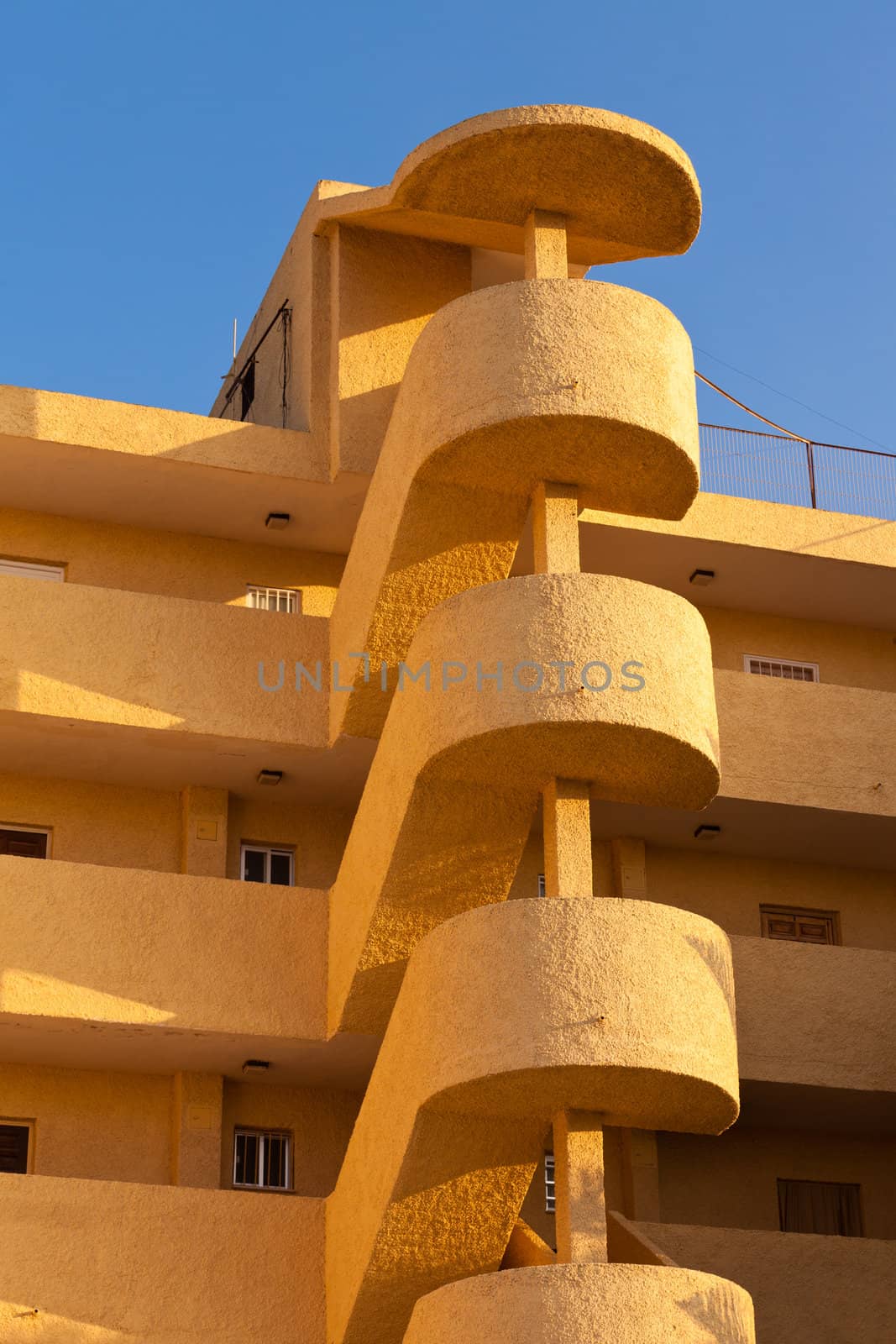 Exterior spiral staircase apartement block architectural feature on multistorey colorful yellow-orange modern condo unit in sunshine of Spain