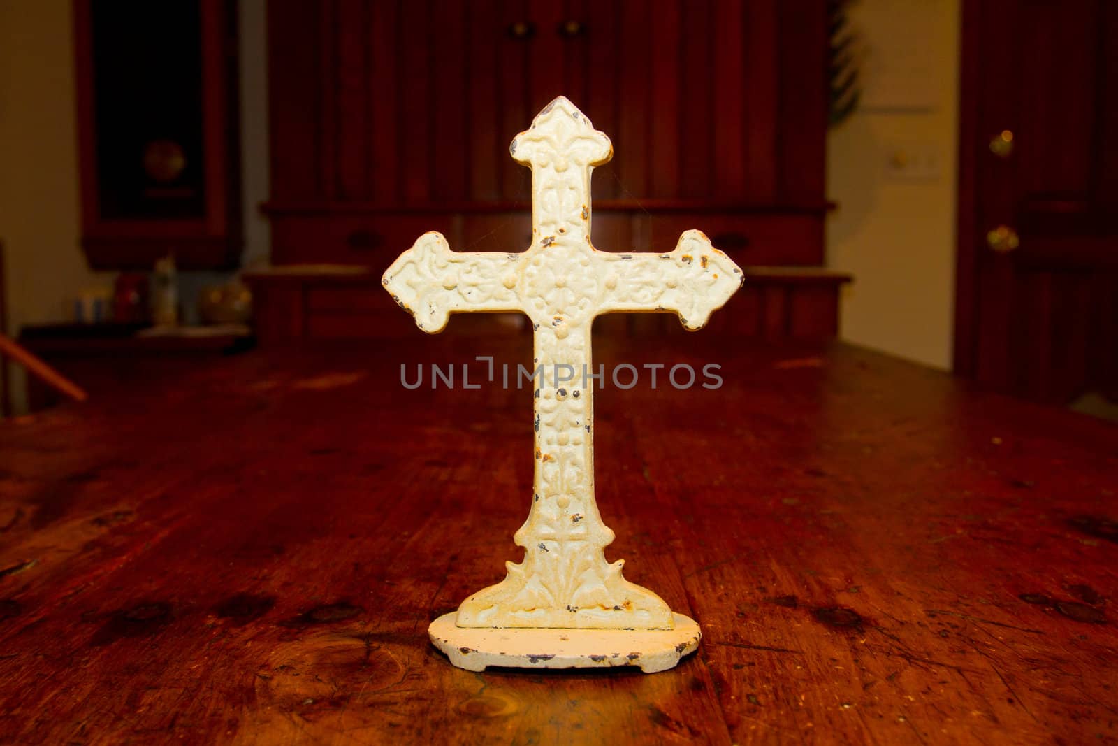 A very old antique white cross photographed on a wood dining table.