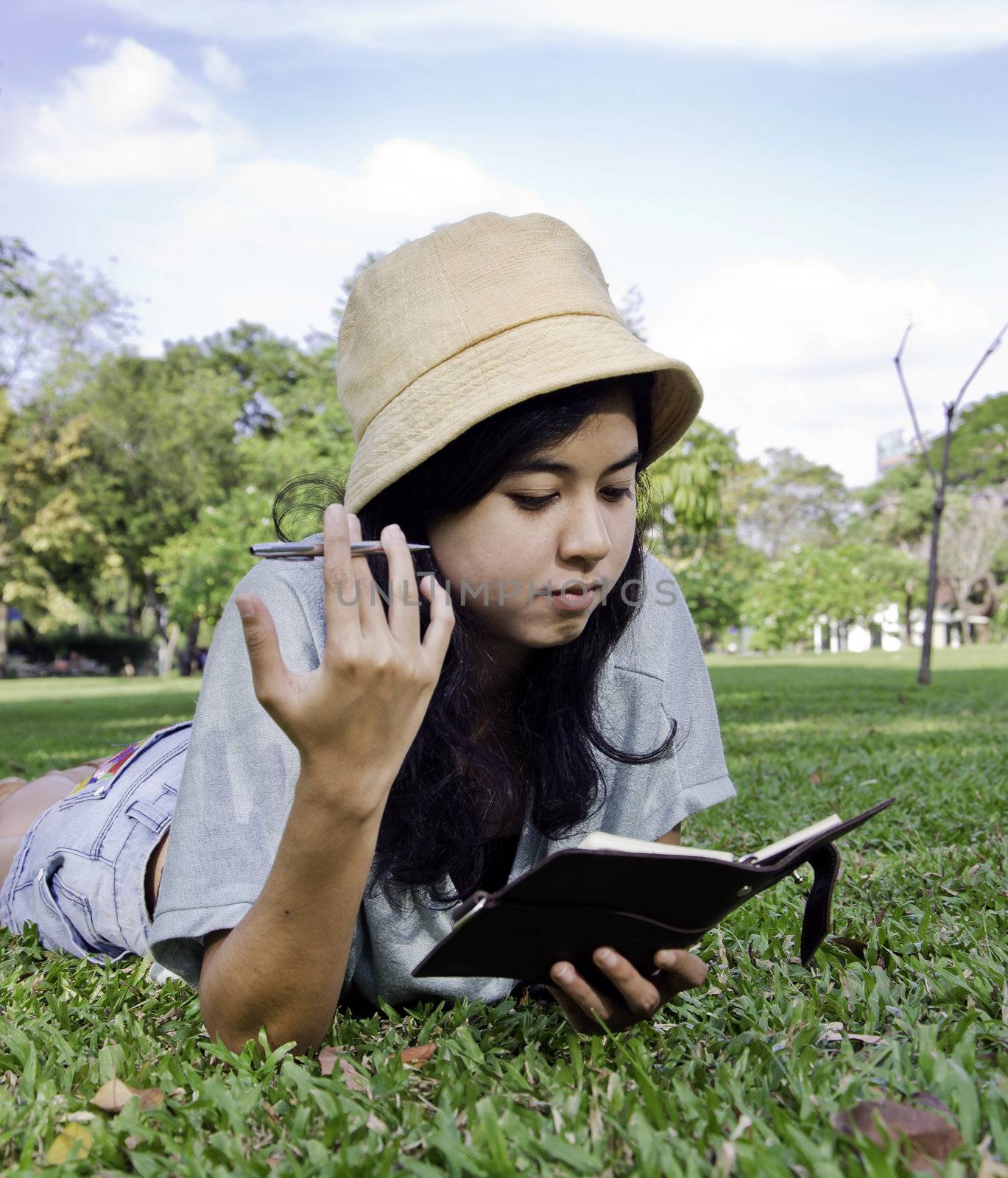 Young beautiful asian woman lies on green summer meadow with book 