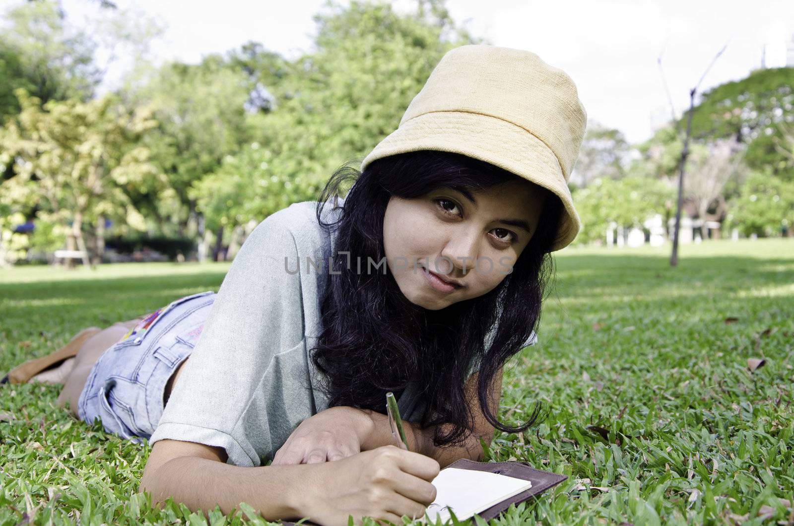 Young woman lies on green summer meadow with book  by siraanamwong