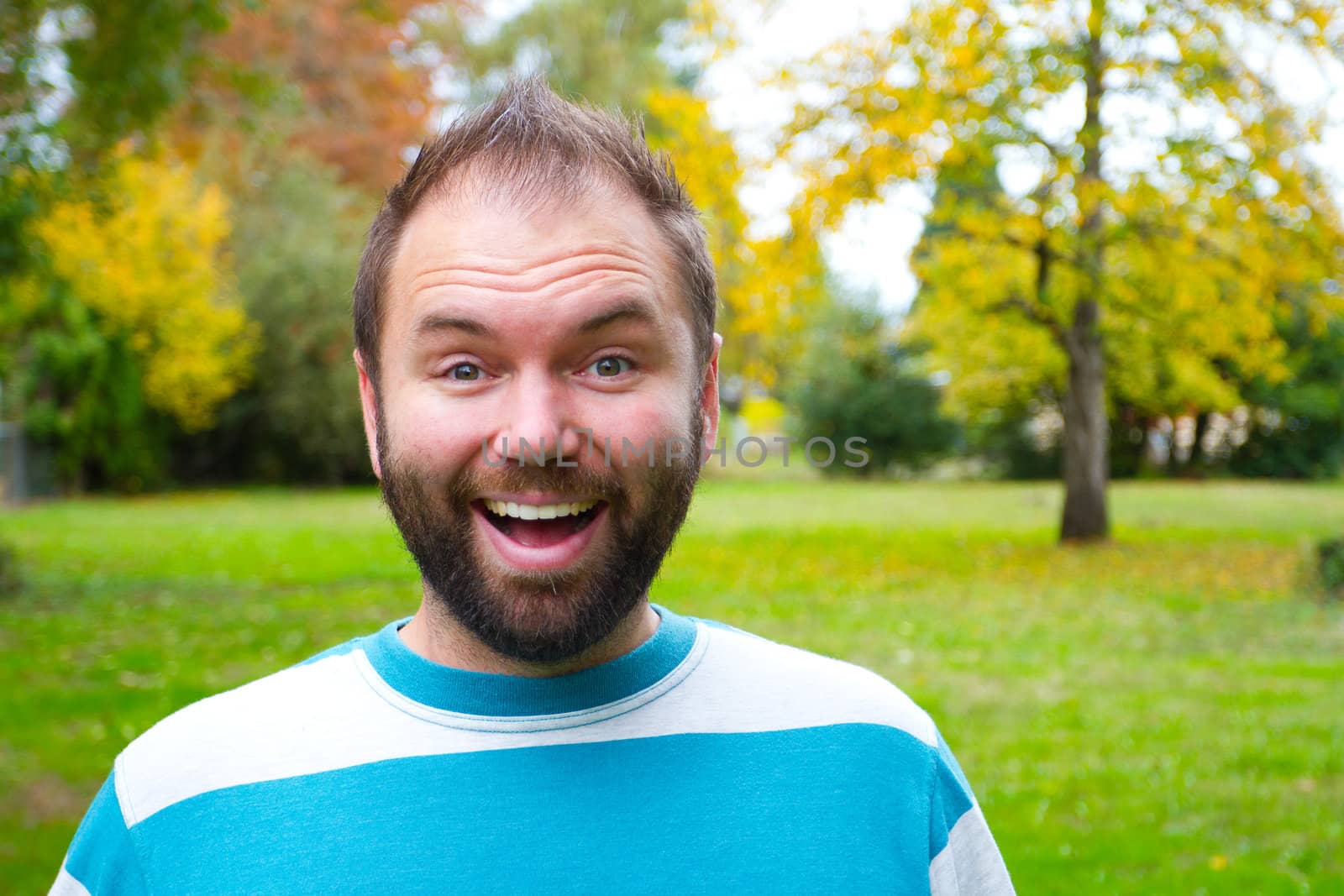 A portrait of a smiling man with a full beard outdoors in a park setting.