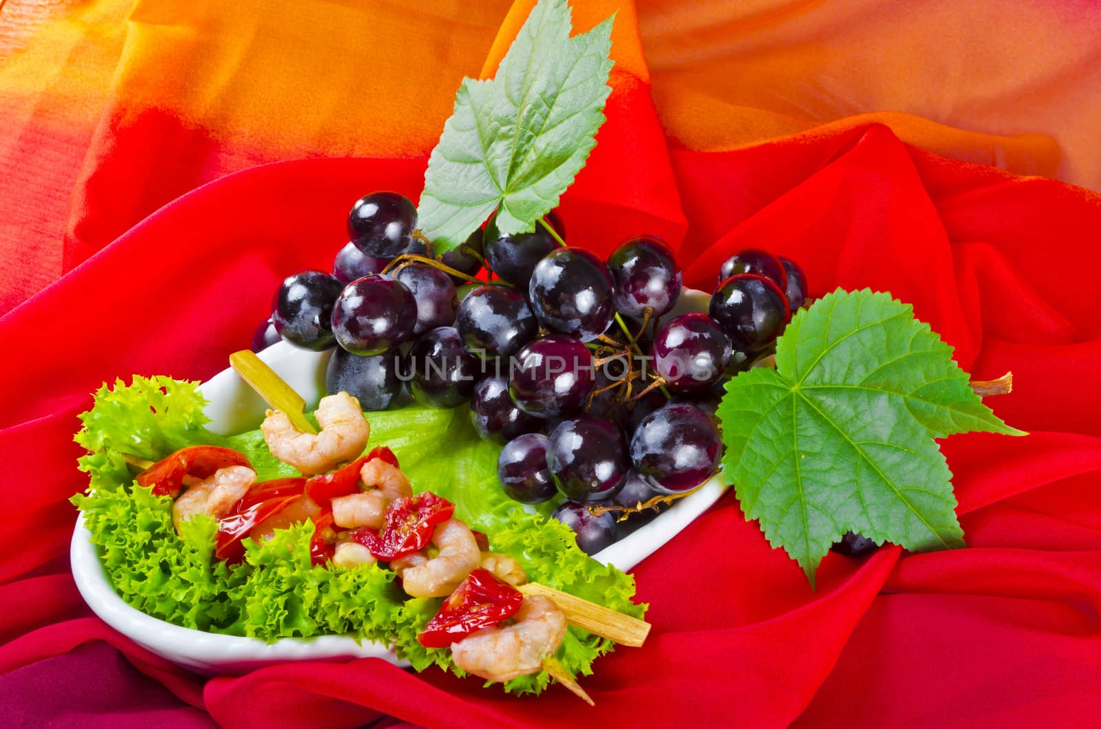 Grilled shrimp spits with bunches of grapes, tomatoes and green salad