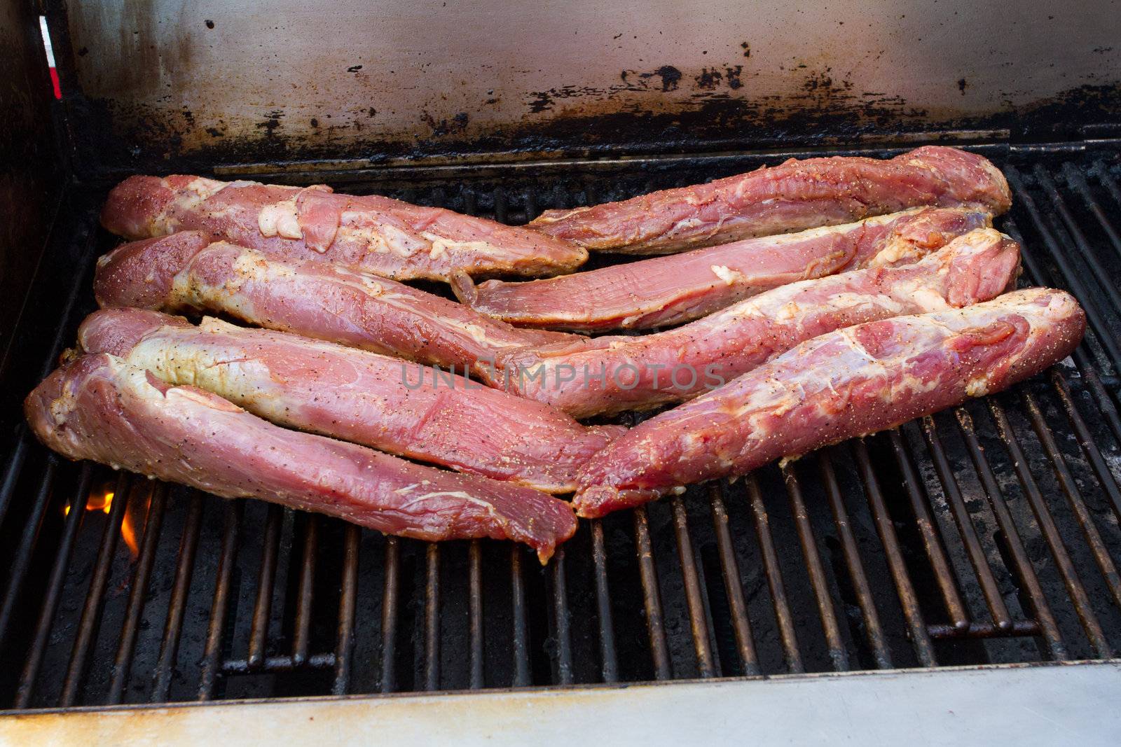 A few slabs of pork are being cooked on a grill barbeque before a wedding.