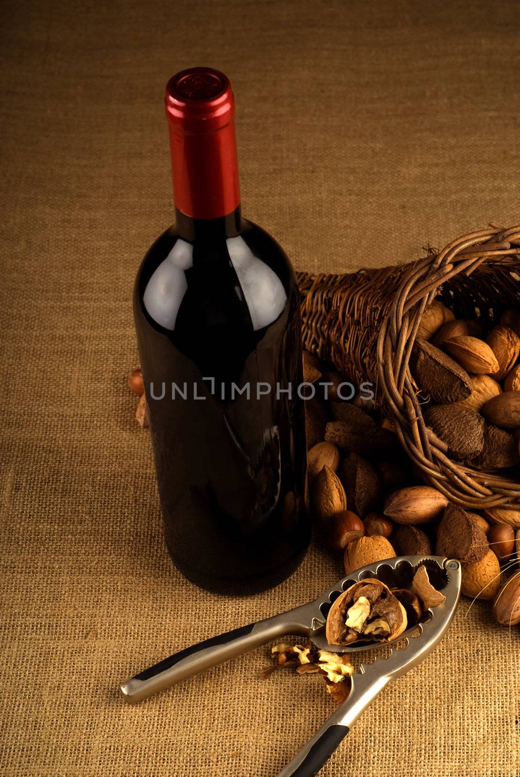 Assortment of nuts in basket with red wine bottle and nutcracker on brown background