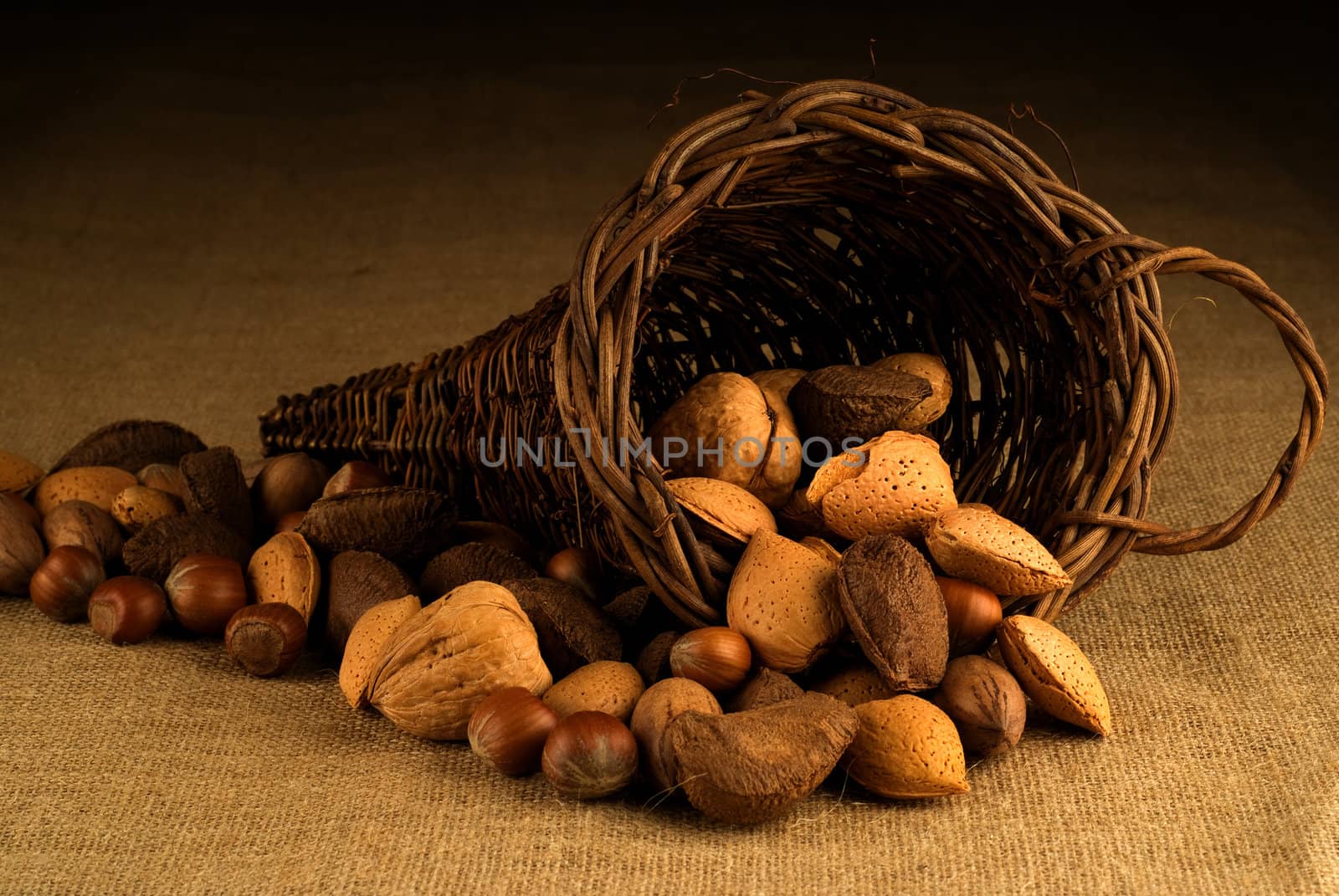 An assortment of nuts overflowing a basket on hesian background