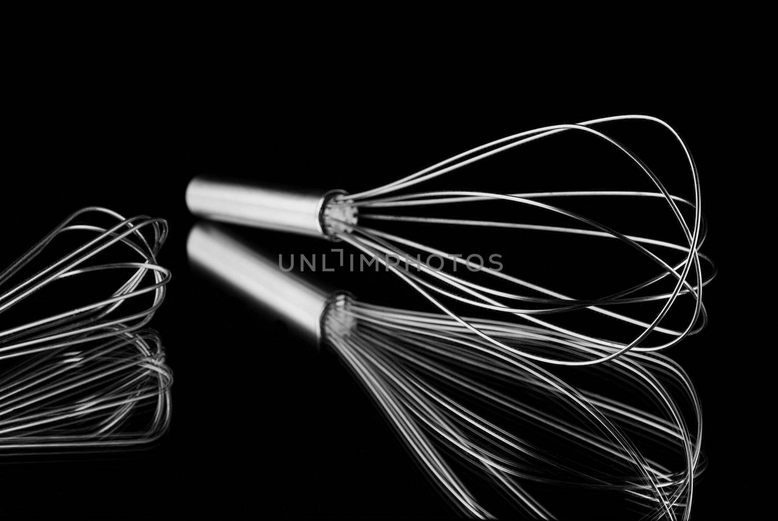 Different sized whisks reflecting on mirror with black background