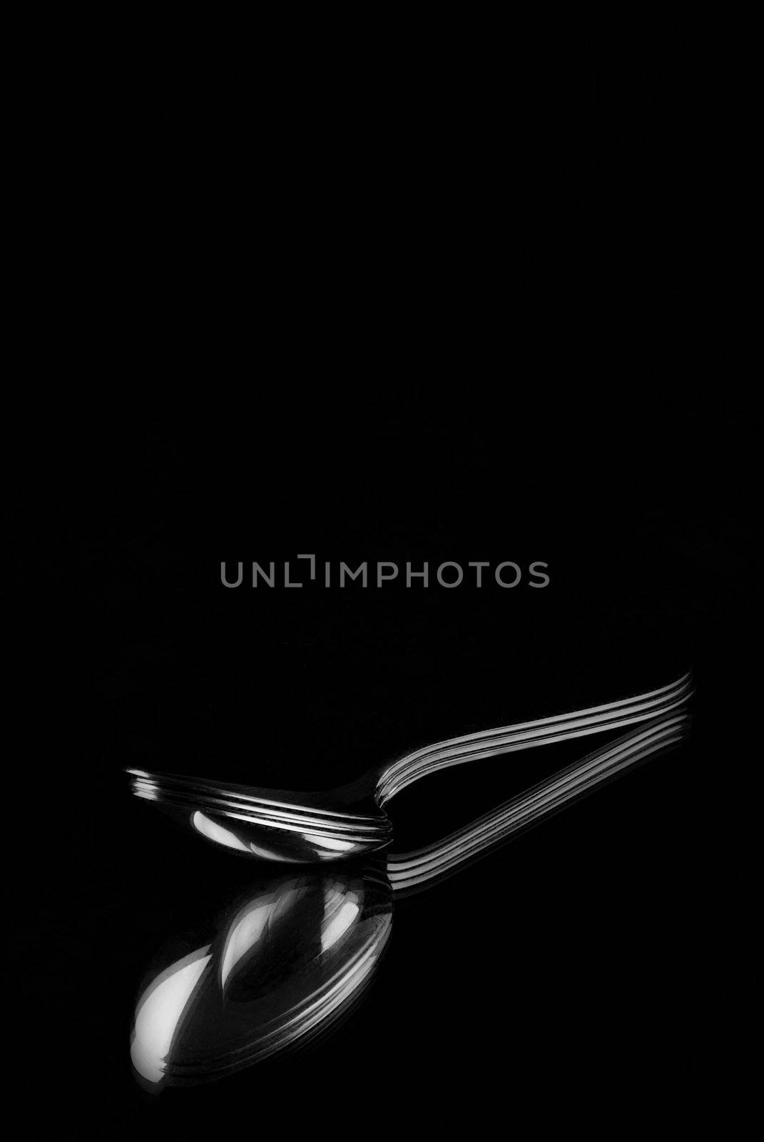 Silver spoons reflecting in mirror with a black background
