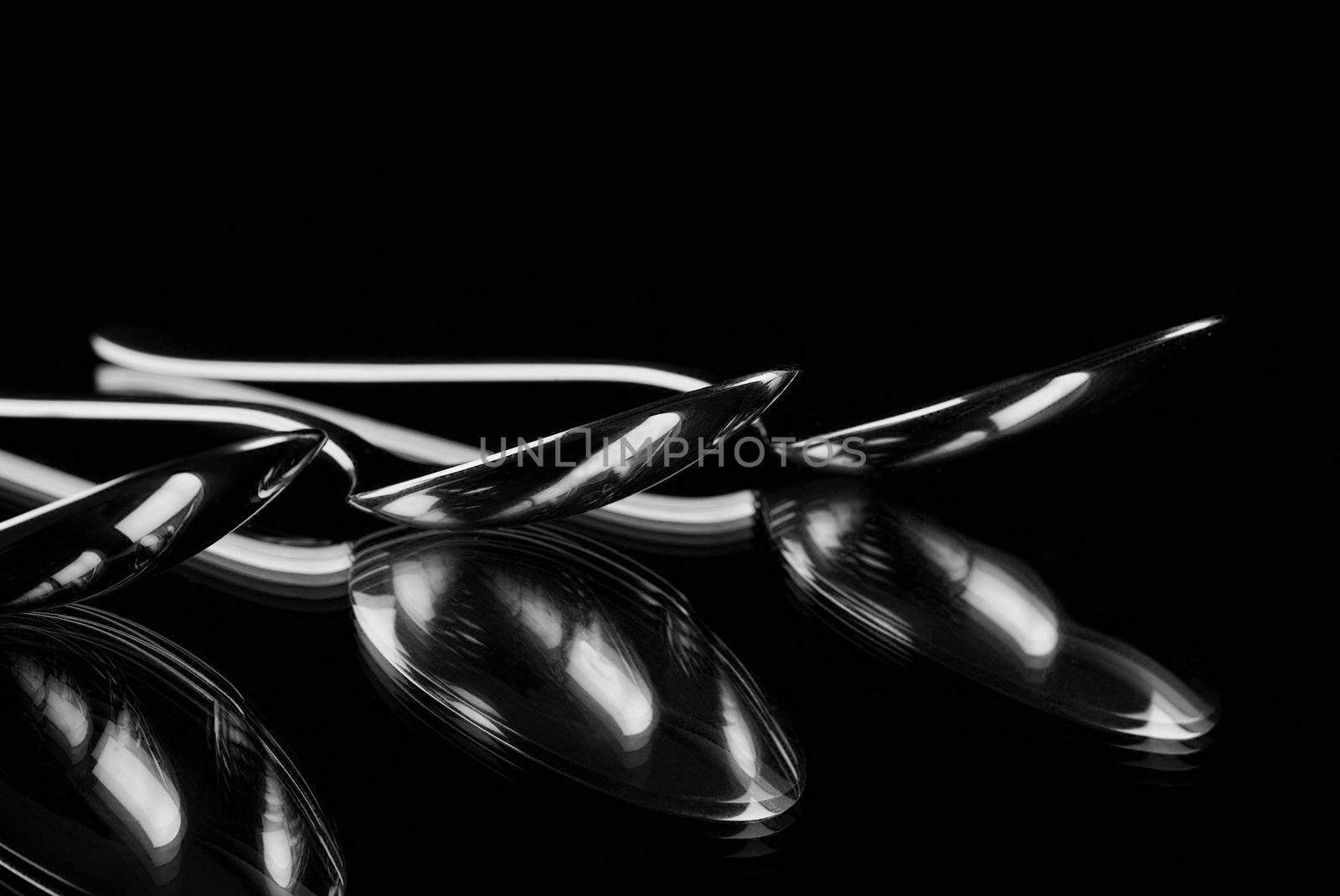 Silver spoons reflecting in mirror with a black background