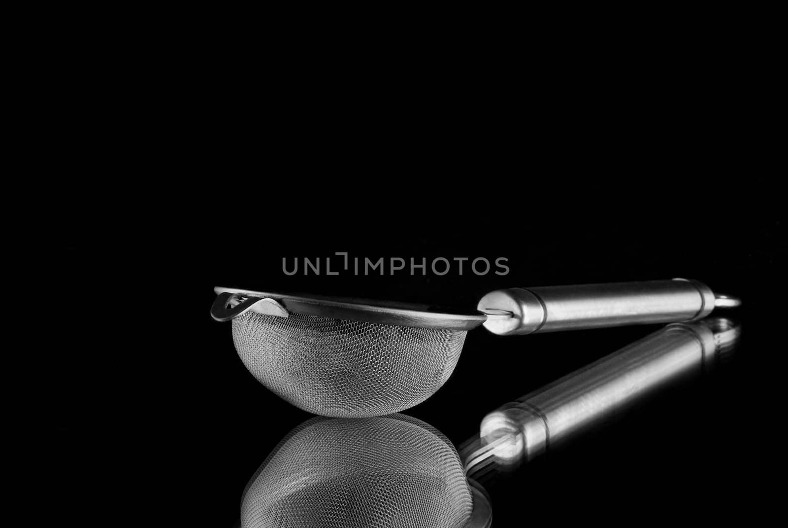 Metal sieve with reflection on mirror with black background