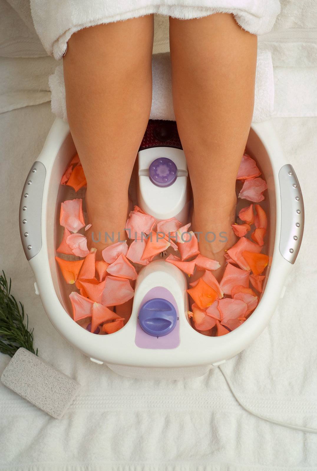 Womens feet in massage spa bath with flower petals