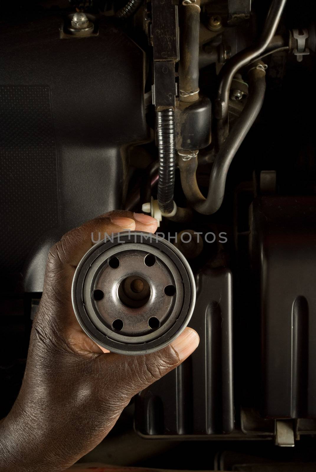 South African or American hand holding oil filter with modern car engine background