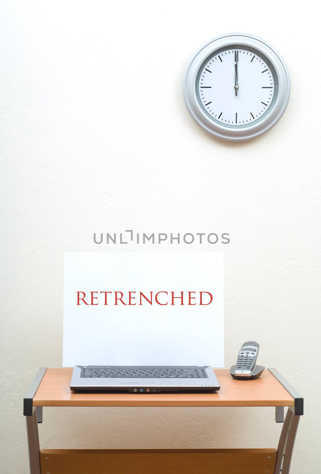 Office desk with retrenched sign on open laptop nest to phone, clock on wall