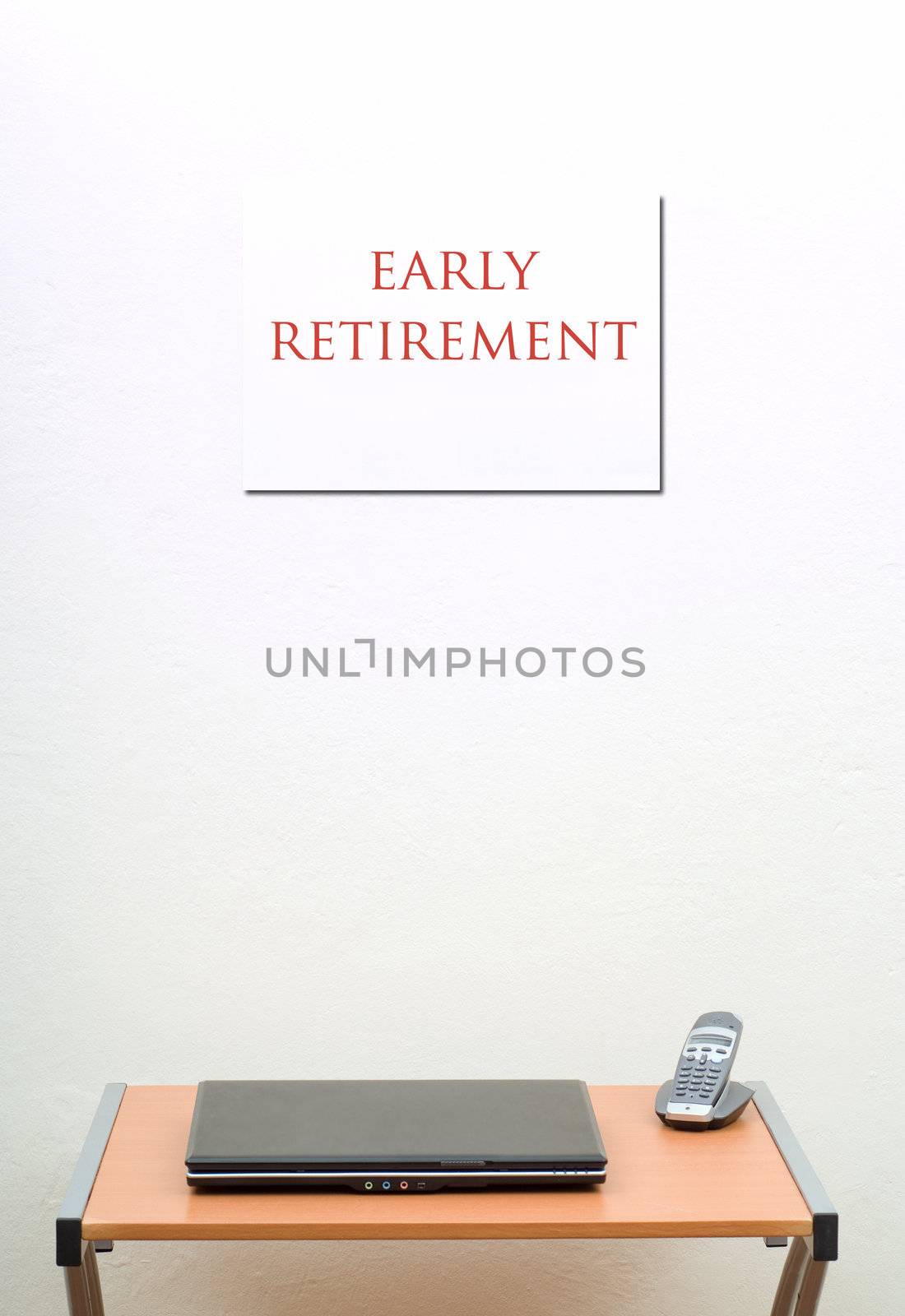 Early retirement sign on wall, office desk, closed laptop with portable phone
