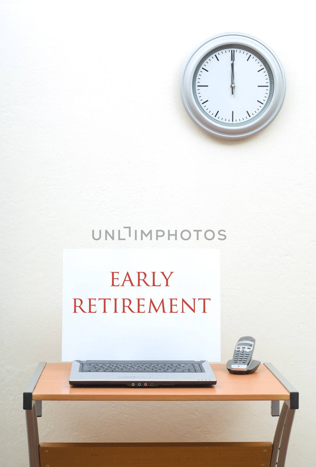 Office desk with early retirement sign on open laptop with portable phone, clock on wall above desk
