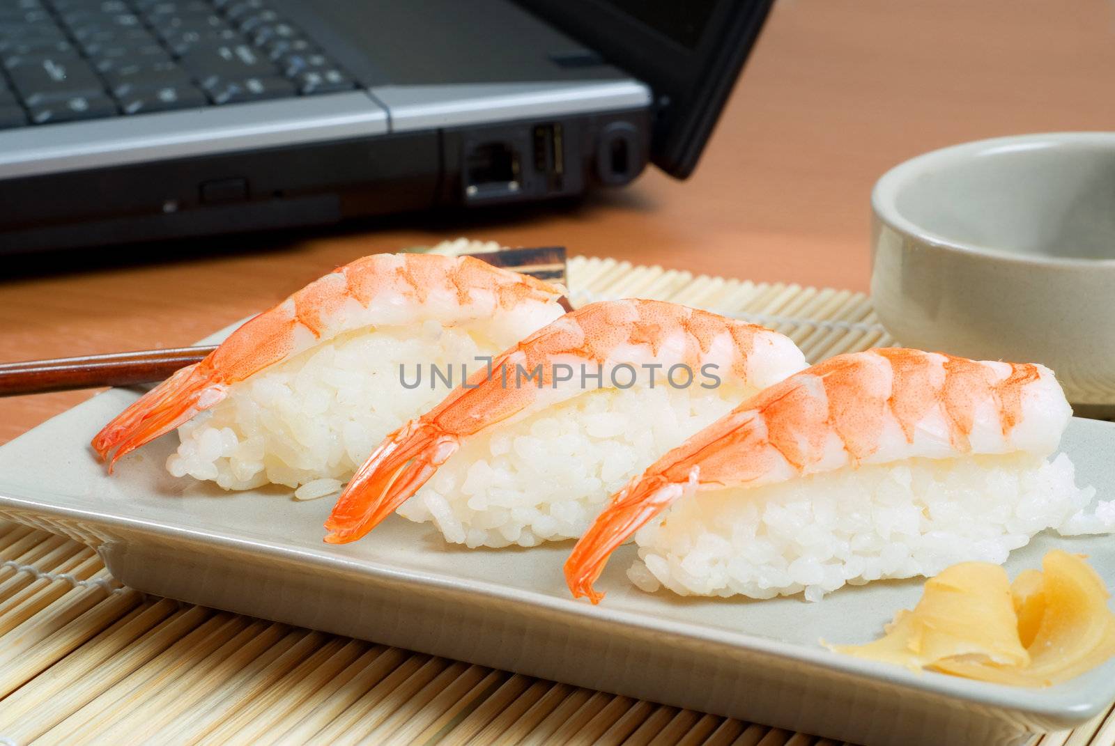 Office business lunch platter of sushi prawn plate with chopsticks, soya sauce and laptop