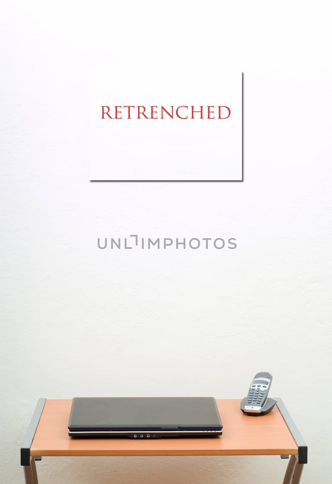 Retrenched sign on wall behind office desk with laptop and phone