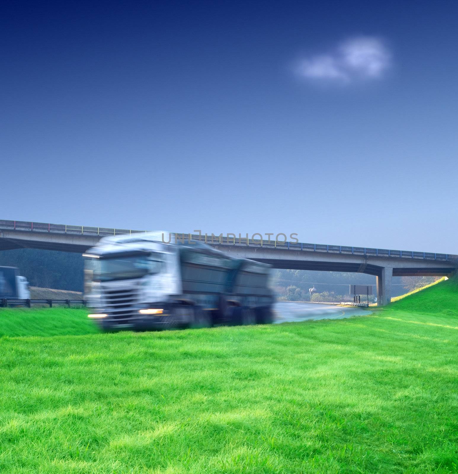Big semi truck delivery load with green grass and blue sky and motion blur