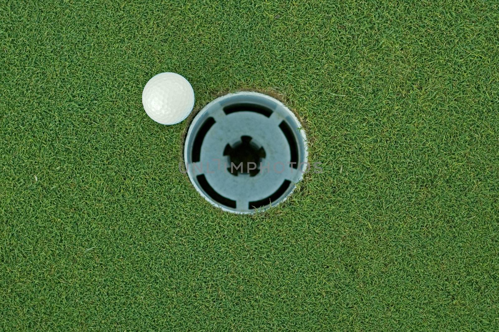 Golf ball on putting green next to hole