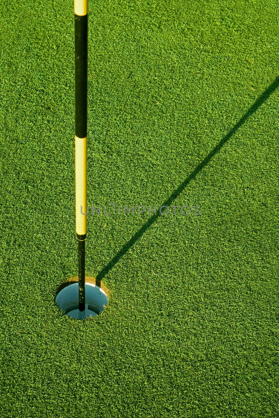 Striped golf flag in green hole with morning shadow on grass