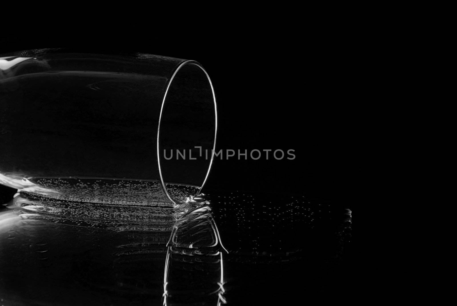 Empty champagne flute lying on it's side reflecting in a mirror with a black background