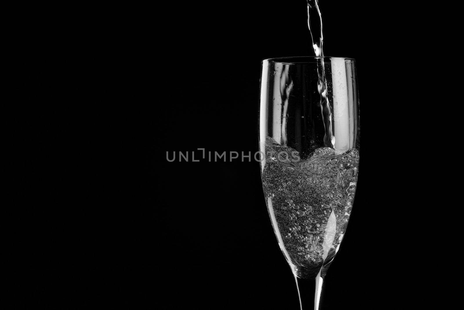 Single flute being filled with sparkling wine on a black background