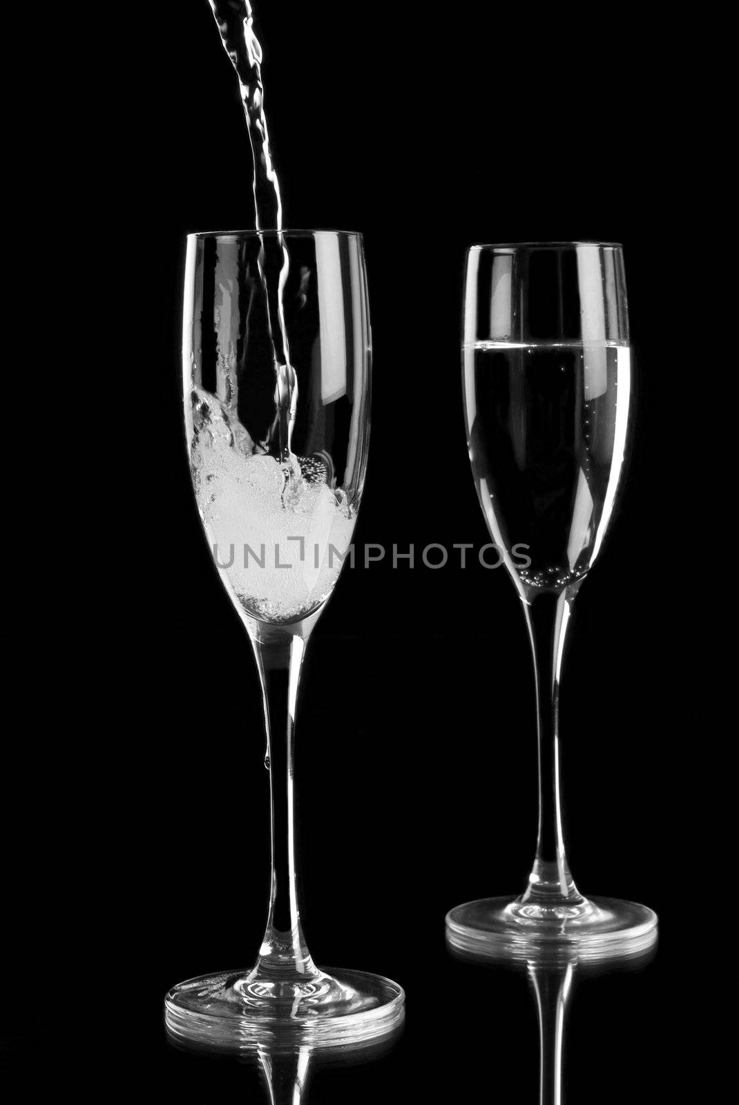 Pouring sparkling wine into champagne flutes on a black background with reflection in a mirror