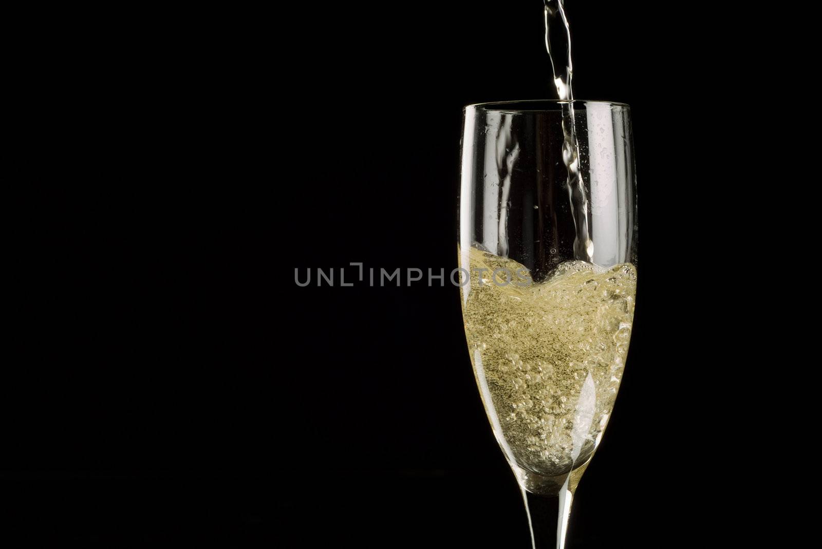 Single flute being filled with sparkling wine on a black background