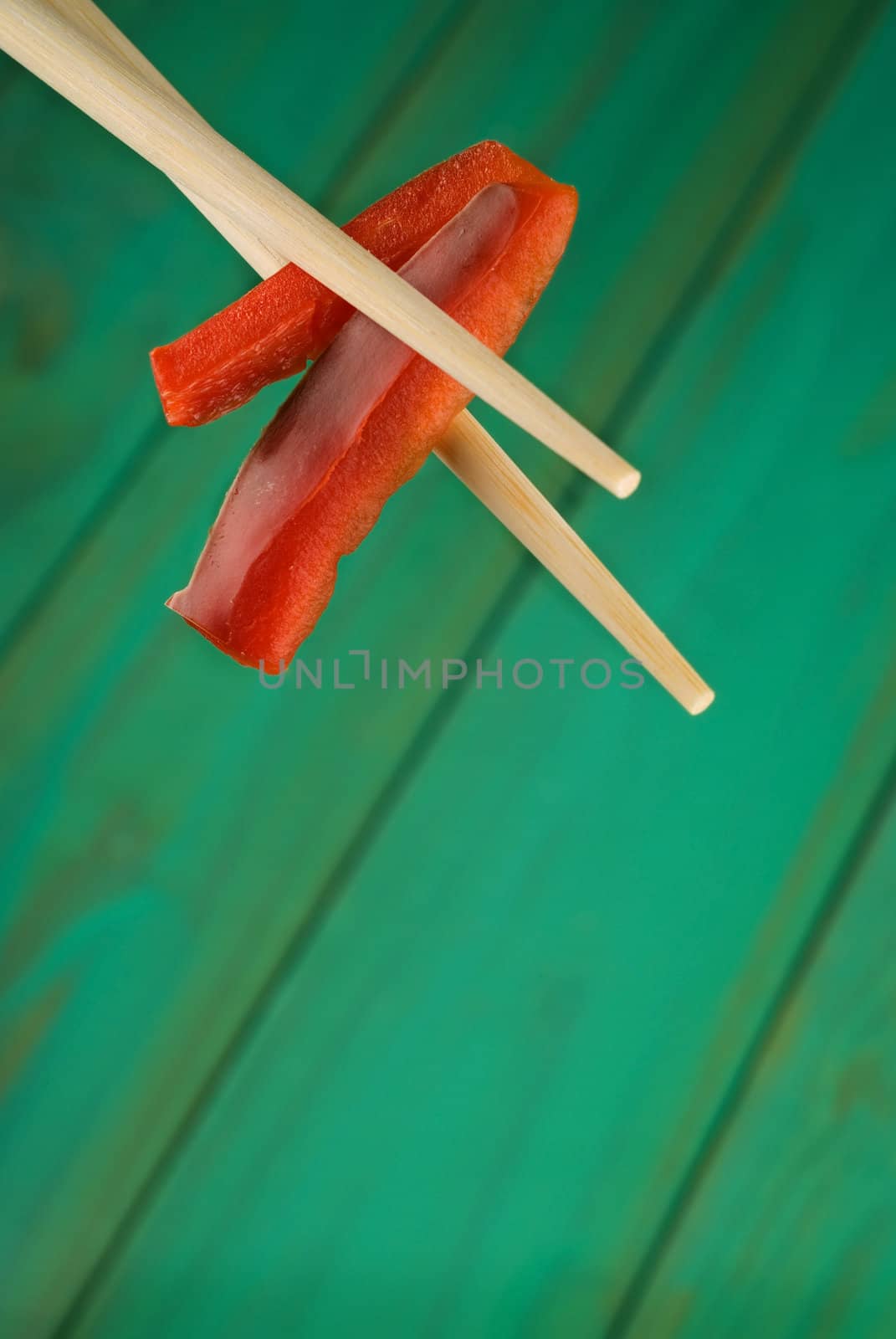 Chopsticks holding two red peppers over wooden table