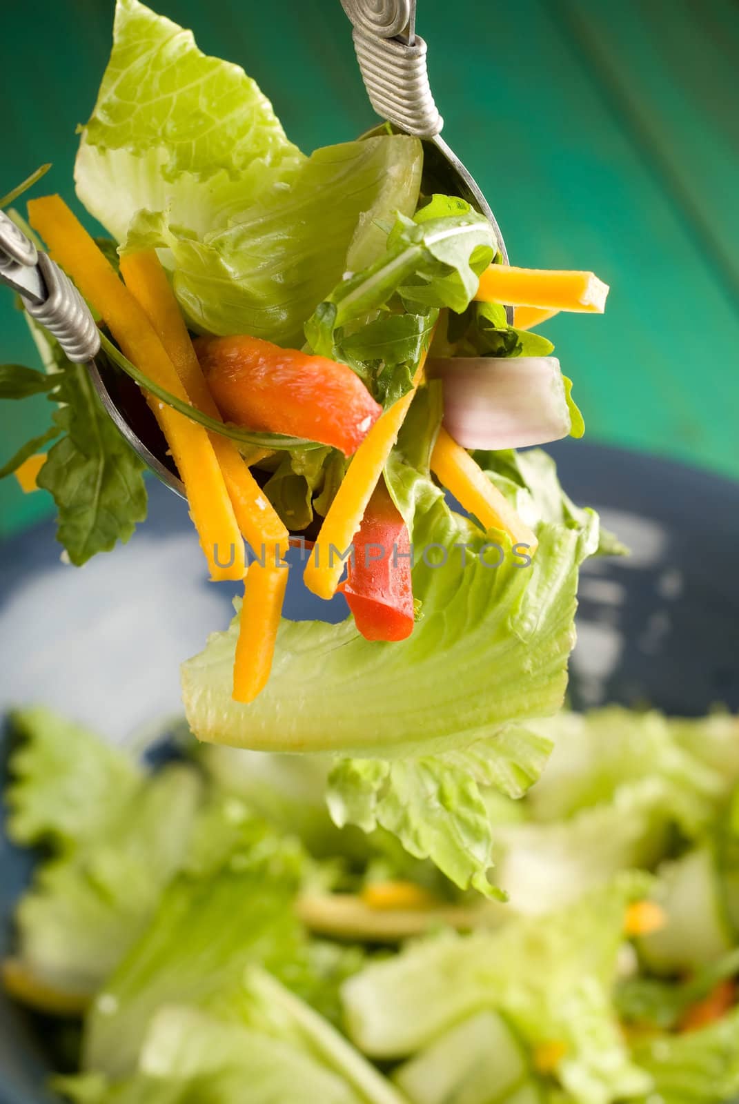 Tossing healthy green salad with server spoons