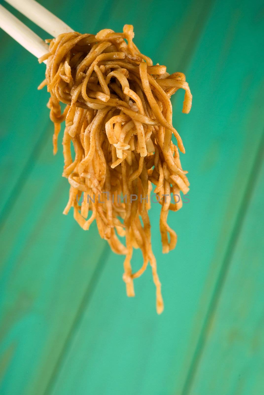 Chopsticks holding noodles over wooden table