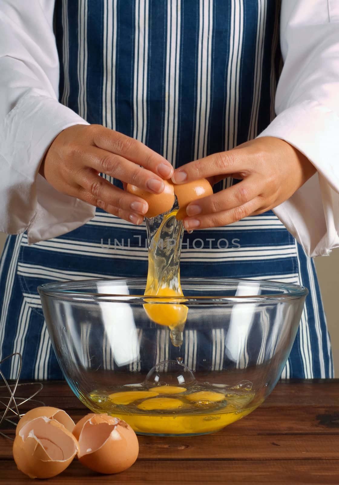 Woman chef or cook breaking egg into kitchen mixing bowl