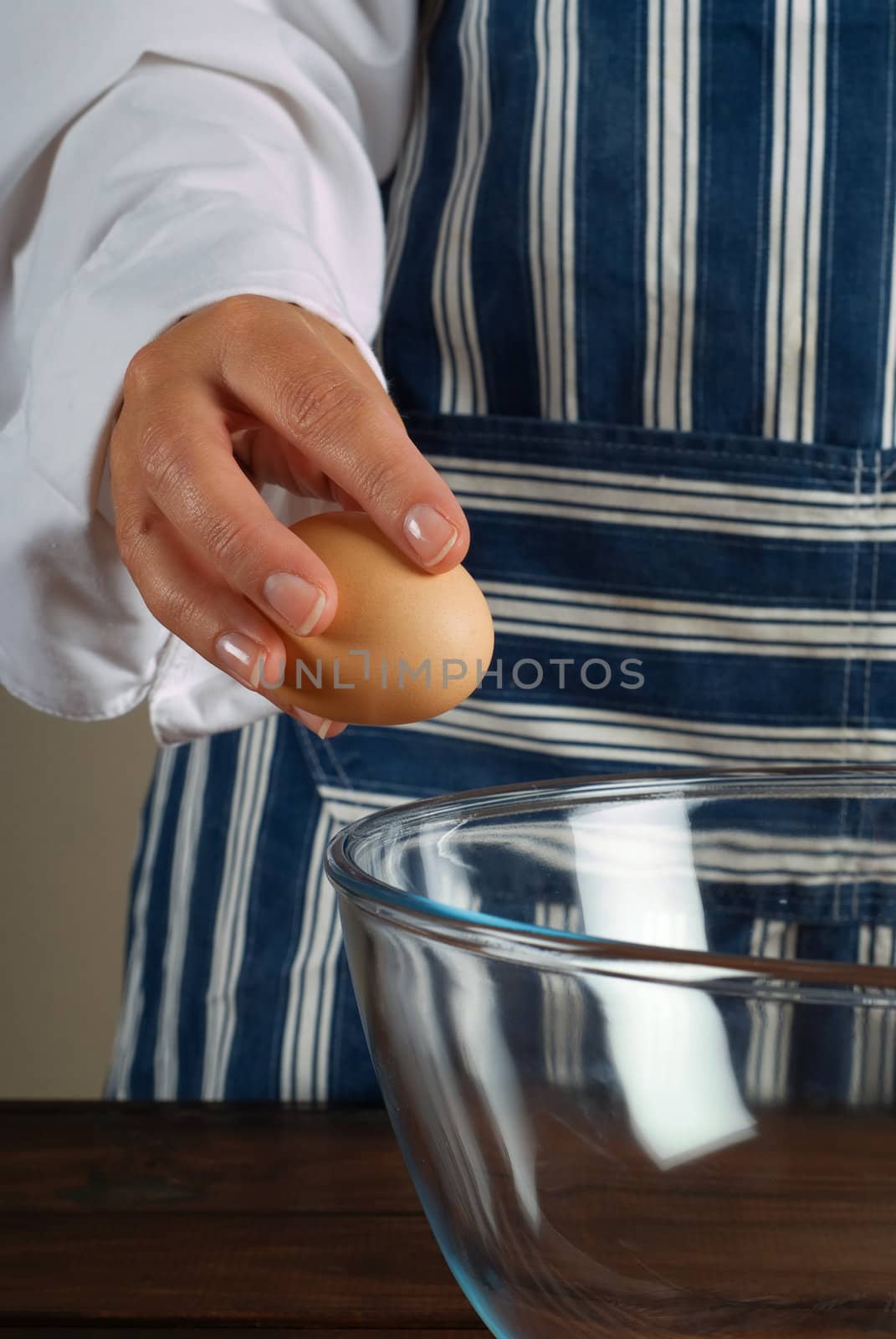 Woman chef or cook breaking egg into kitchen mixing bowl