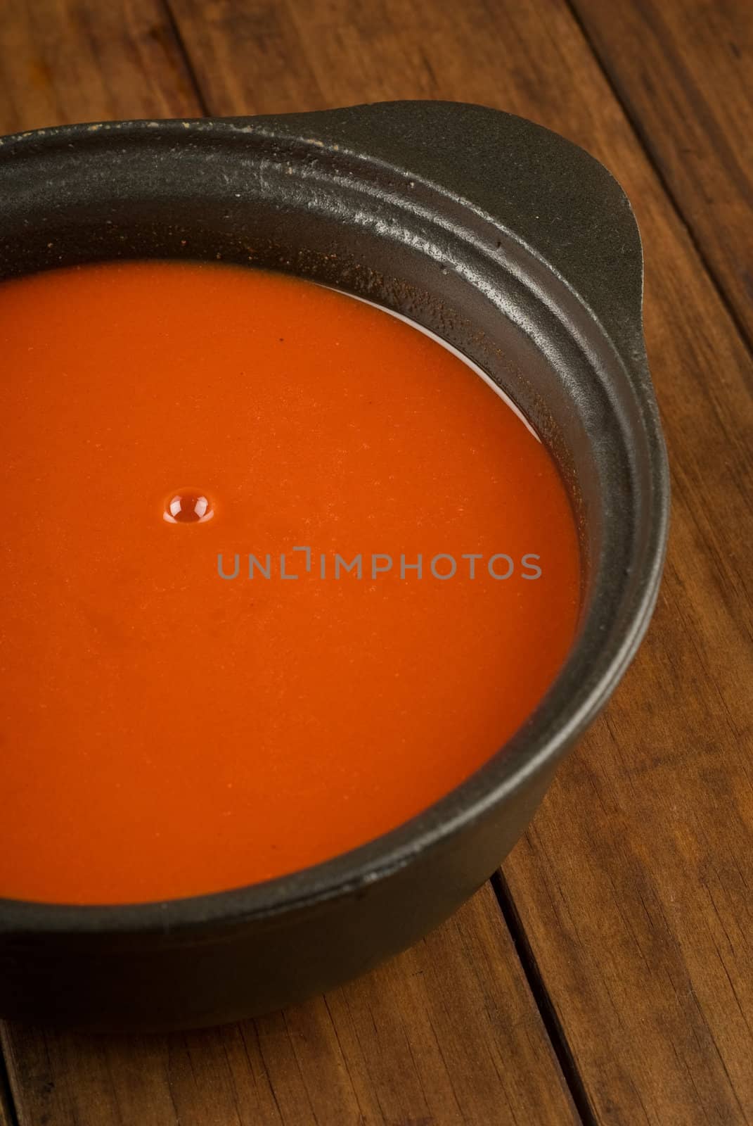 Fresh tomato soup with bubble in black pot on wooden table