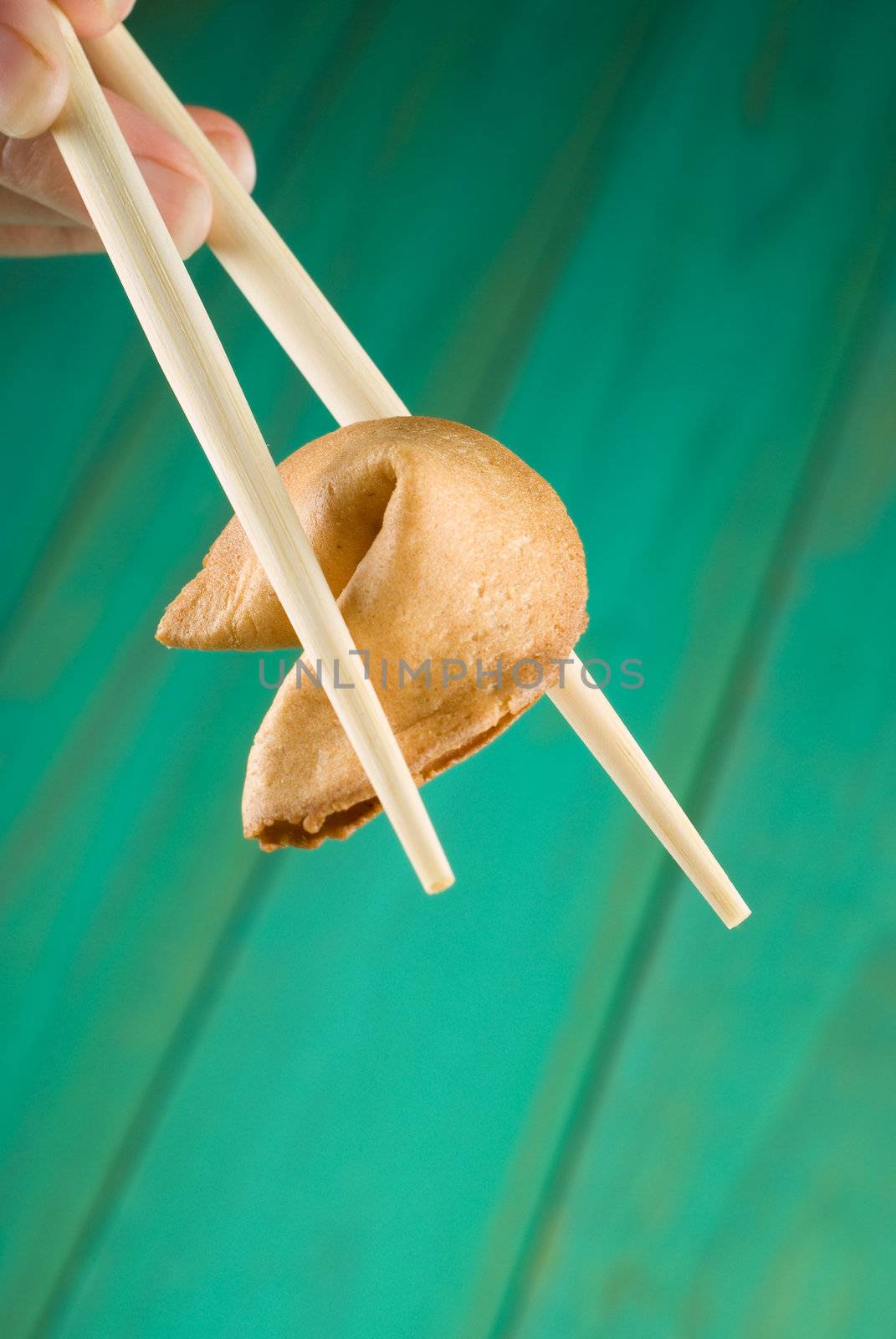 Chopsticks holding fortune cookie over green table