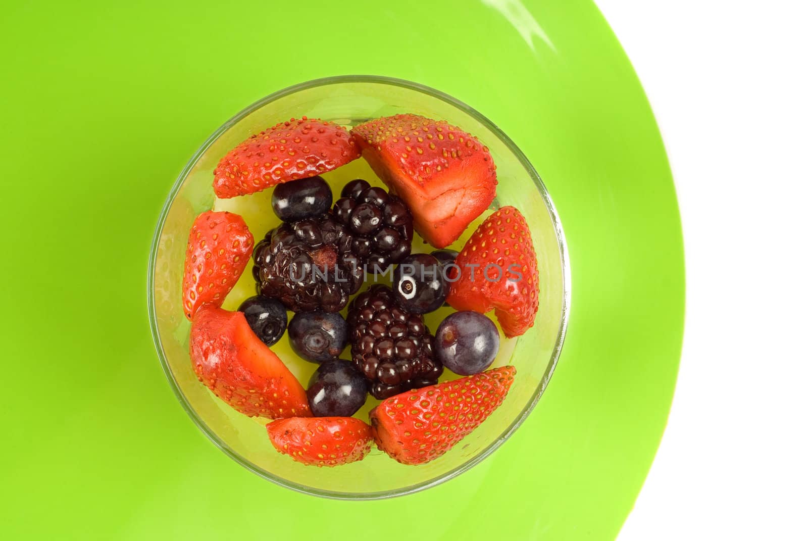 Glass of strawberries and other berries on green plate