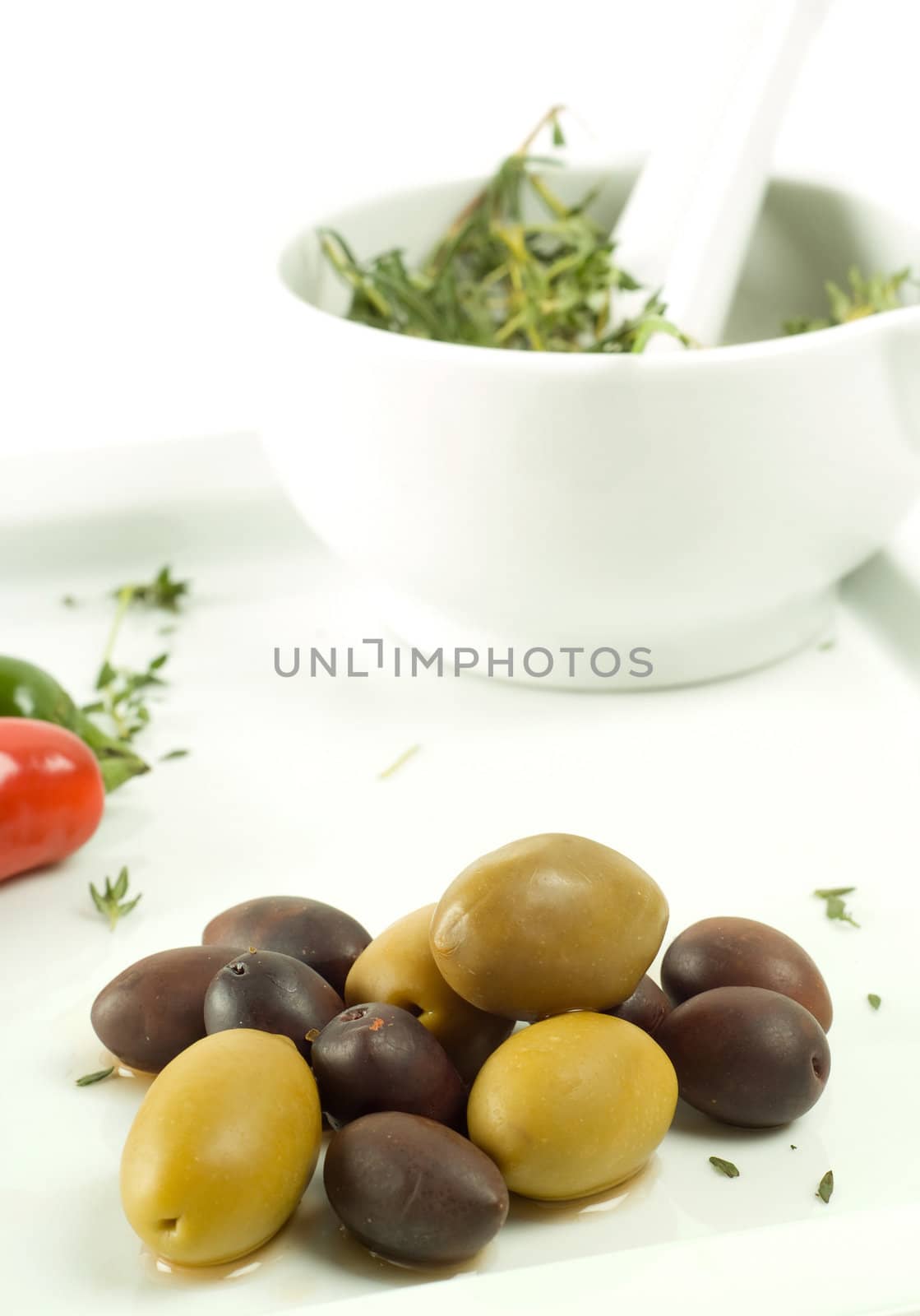 Mortar and pestle with herbs and chili or chilli vegetable food with olives on white