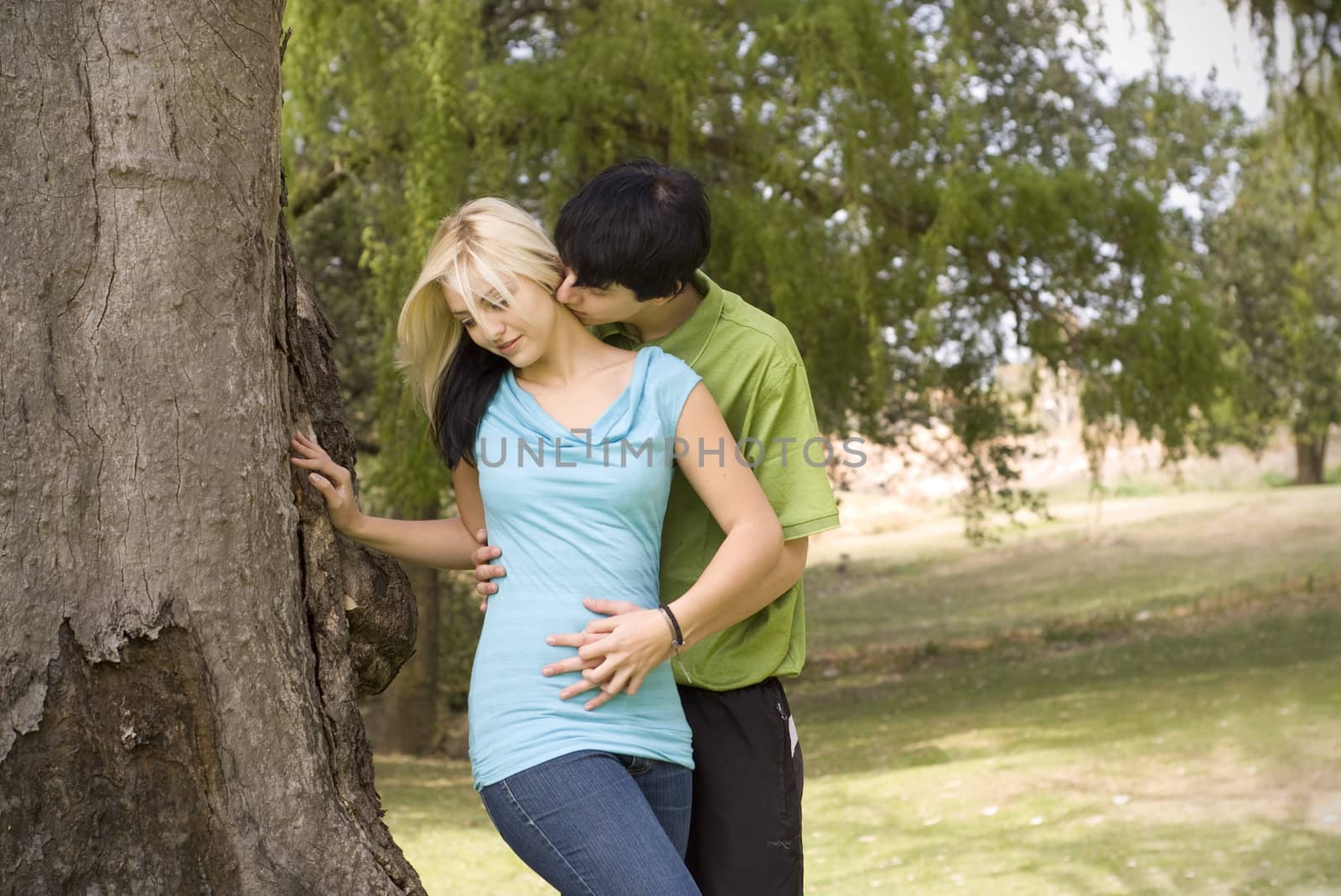 Boyfriend kissing girlfriend neck next to garden tree