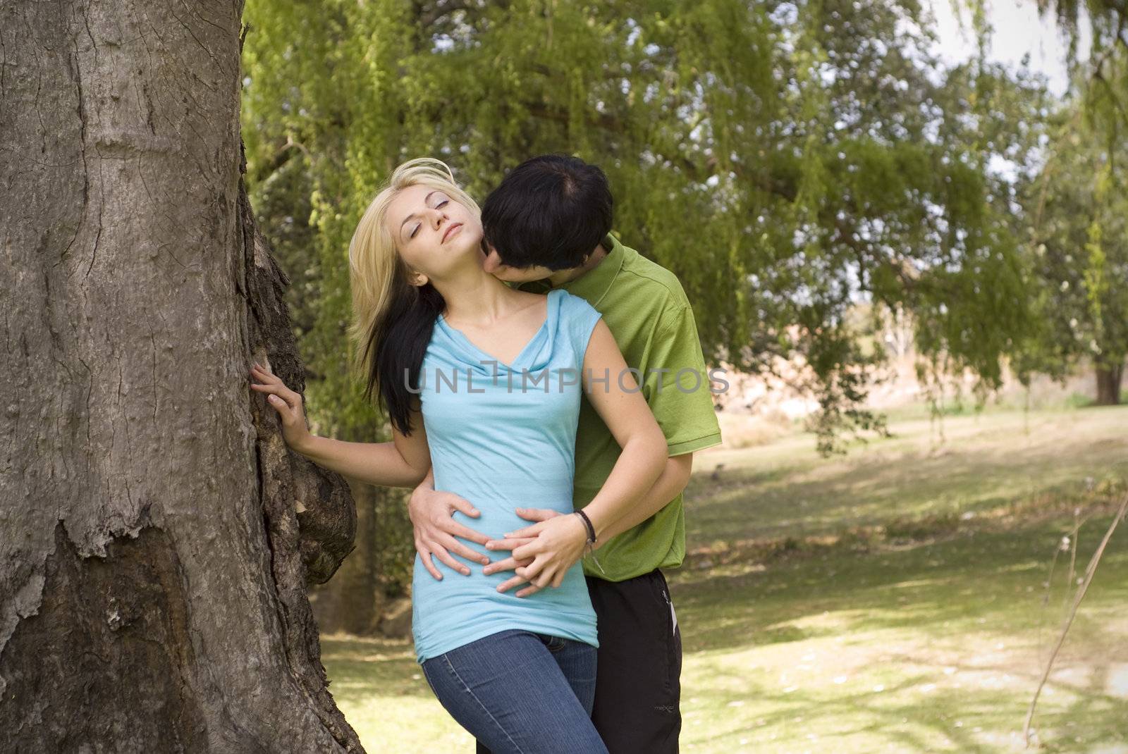 Boyfriend kissing girlfriend on neck in garden with tree