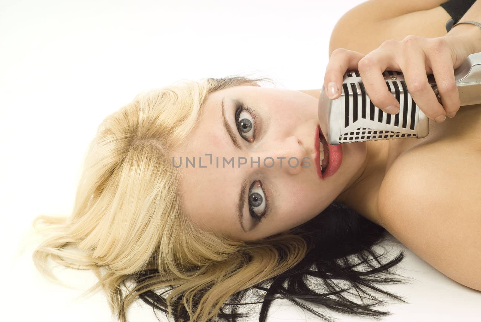 Portait of pretty woman or girl music singer lying down with microphone on white