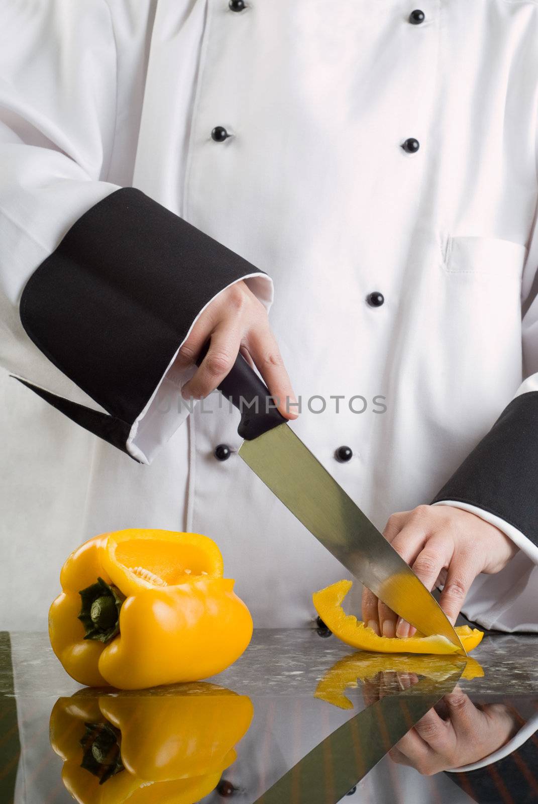 Chef in Black and White Uniform Cutting a Yellow Pepper Reflecting in Stove Top