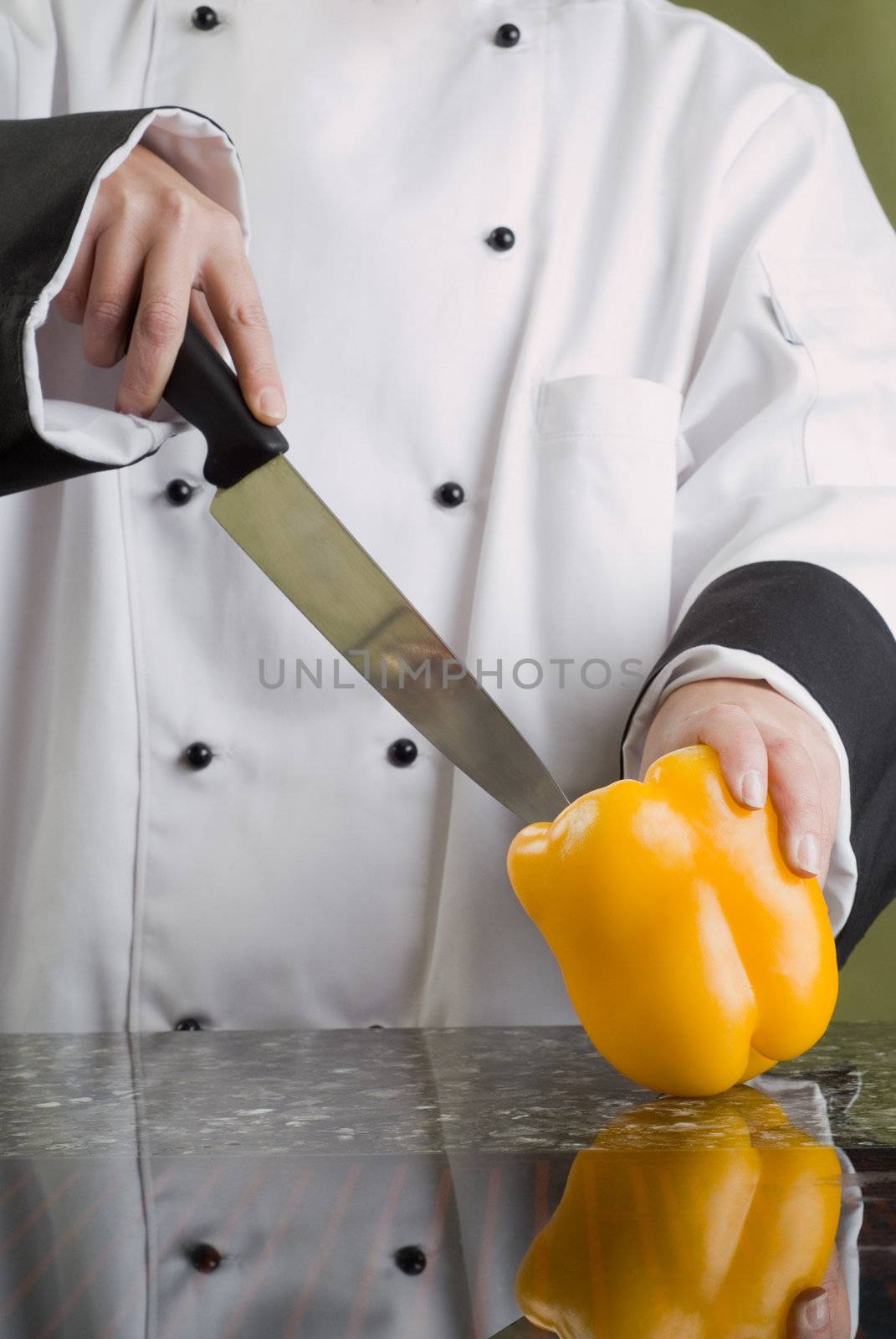 Chef in Black and White Uniform Cutting a Yellow Pepper Reflecting in Stove Top