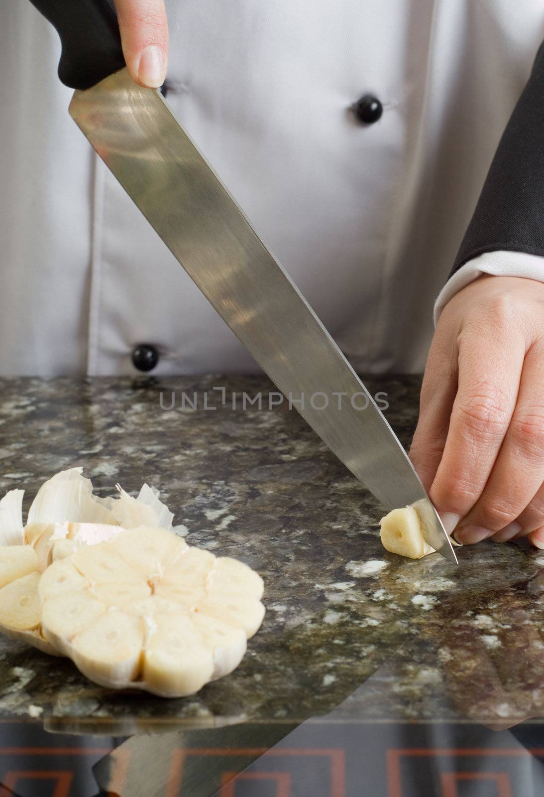 Chef Wearing Black and White Uniform Slicing Clove of Garlic