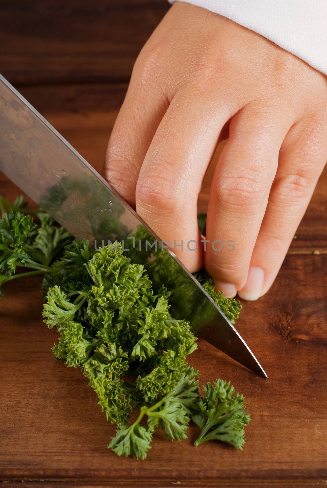 Woman cook or chef chop or chopping parsley with knife on wooden board