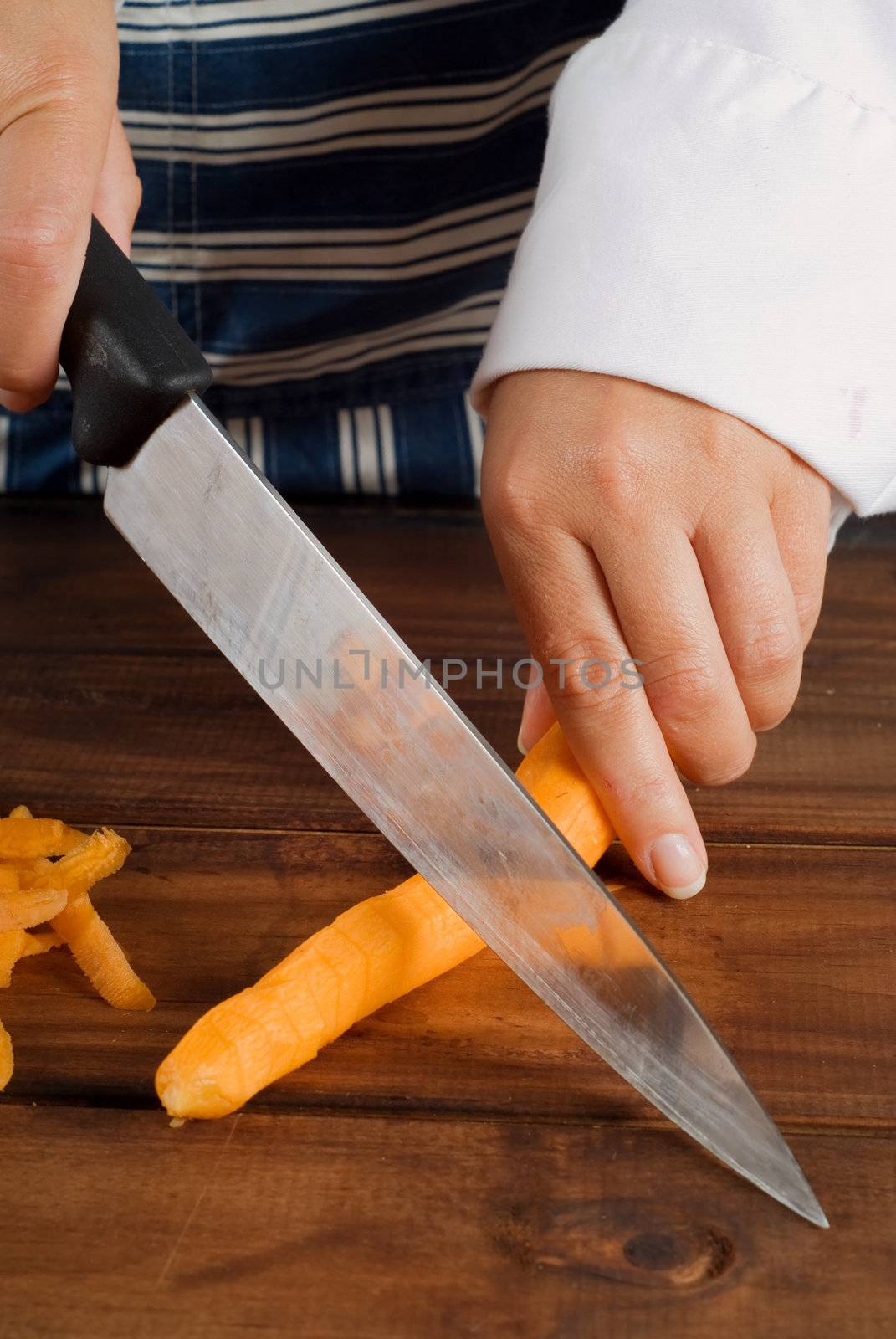 Woman female cook or chef slicing or cutting a carrot with kitchen knife on wooden board