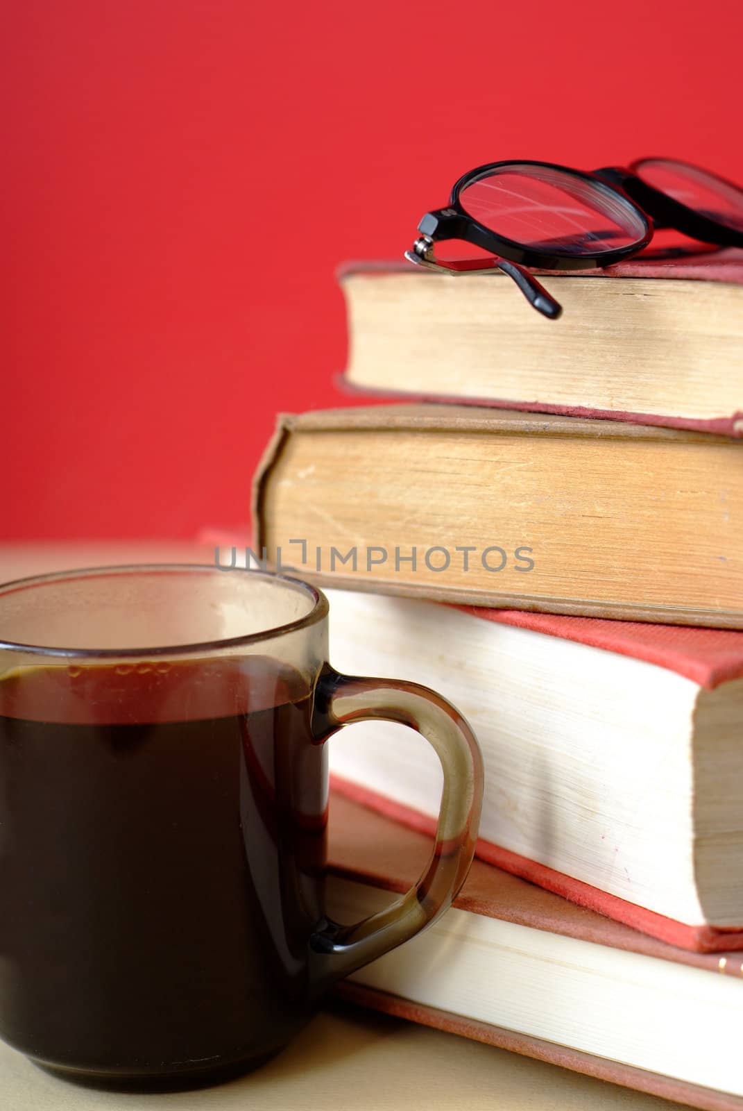 Pile of old books with covers and white pages with red background and a mug or cup of coffee with reading glasses