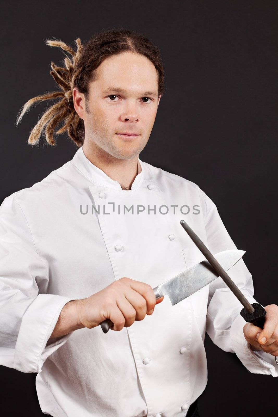 Photo of a chef with dreadlocks sharpening his chopping knife.
